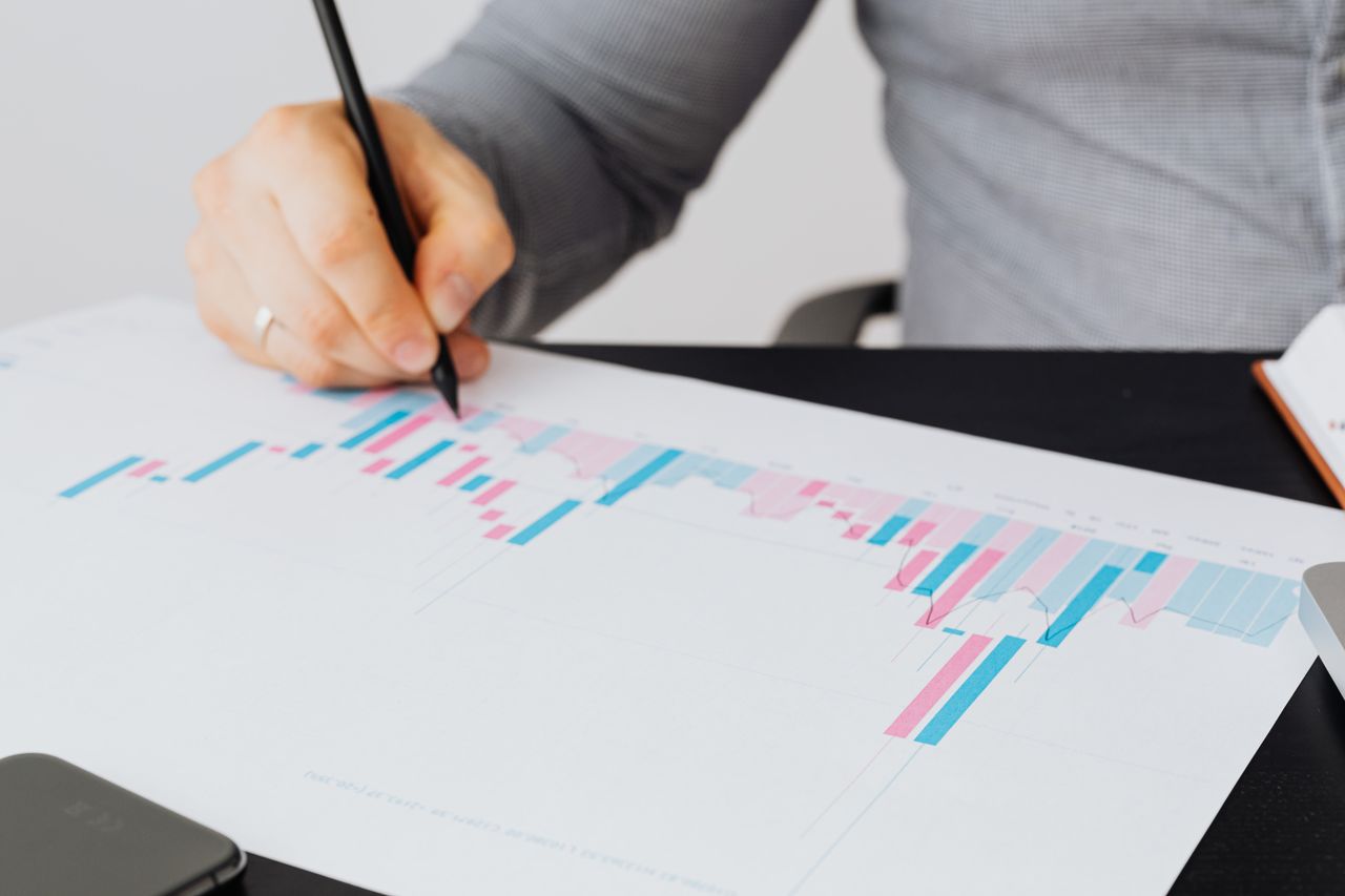 About Close-up of a man writing on a printed chart indoors, analyzing colorful data.