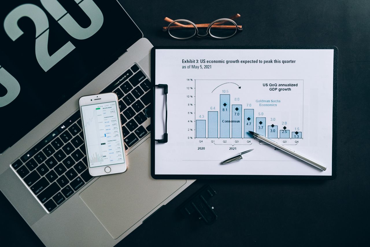 About Top view of a financial data analysis setup with laptop, smartphone, and graph on clipboard.